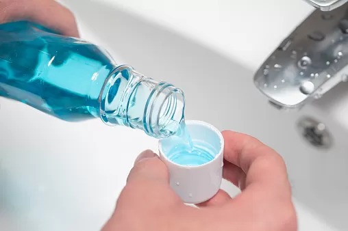 Hand of man pouring bottle of mouthwash into cap.